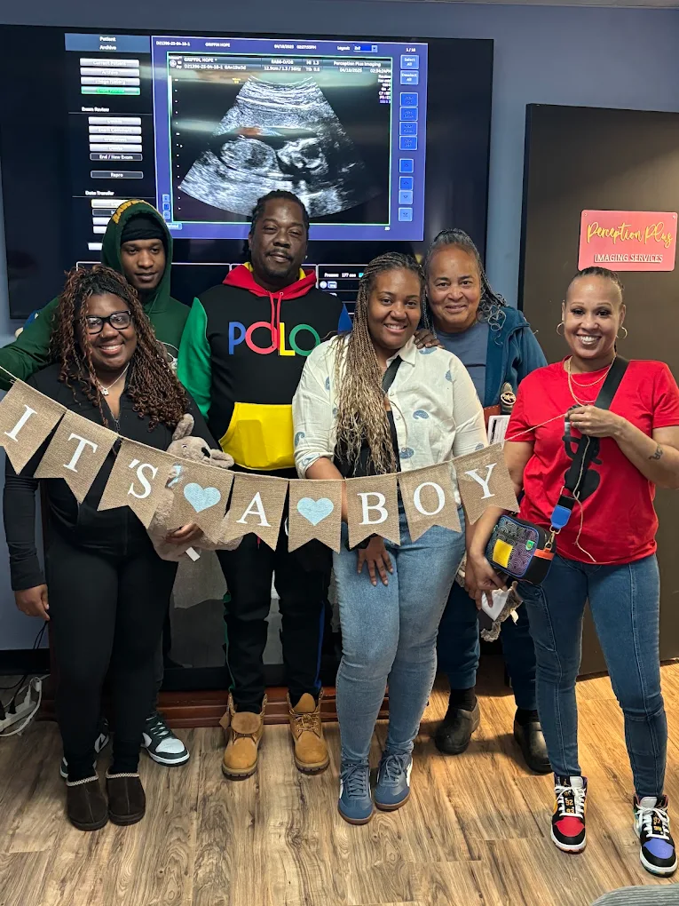 A family holding an It's a Boy banner in front of the scan on the studio's big screen.