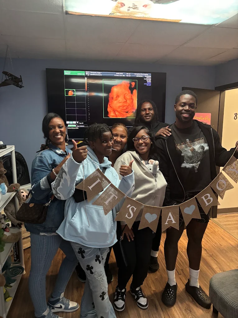 A family cheering with an It's a Boy banner while a 4D scan glows on the screen behind them.