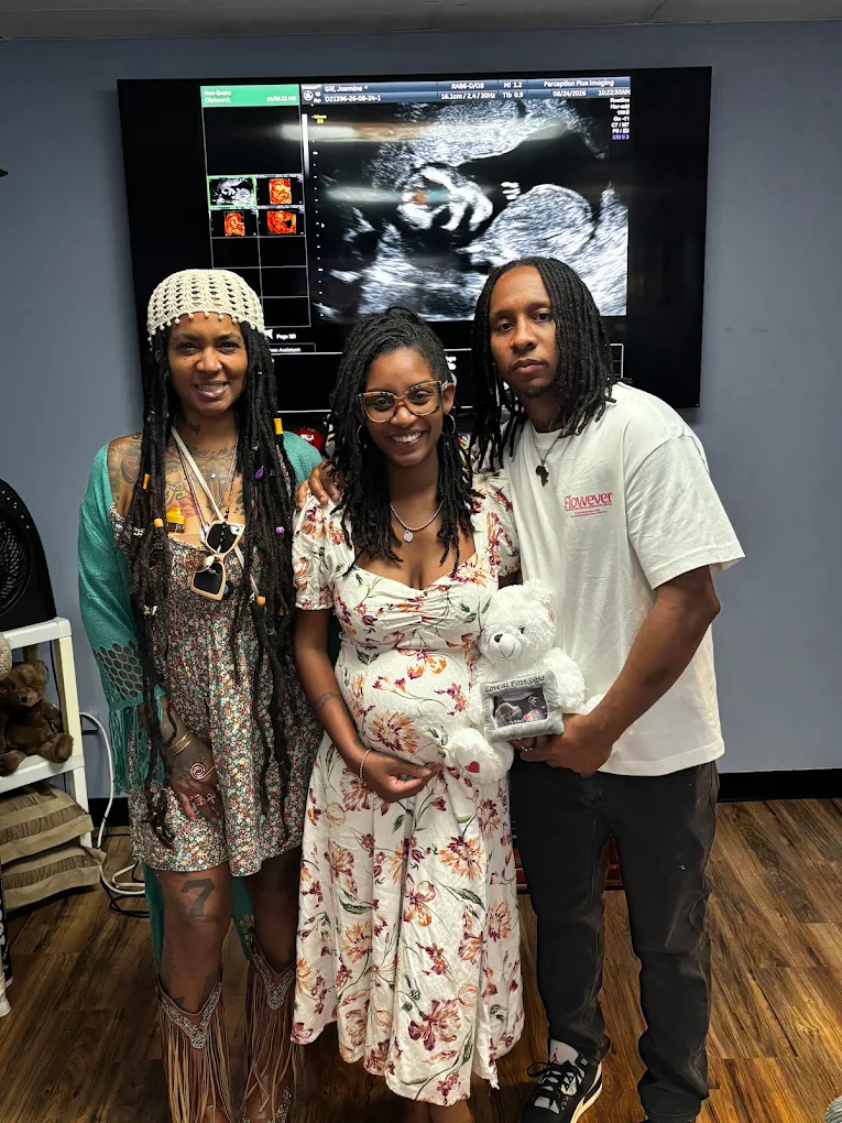 Expectant parents and family with a keepsake bear holding their scan print.
