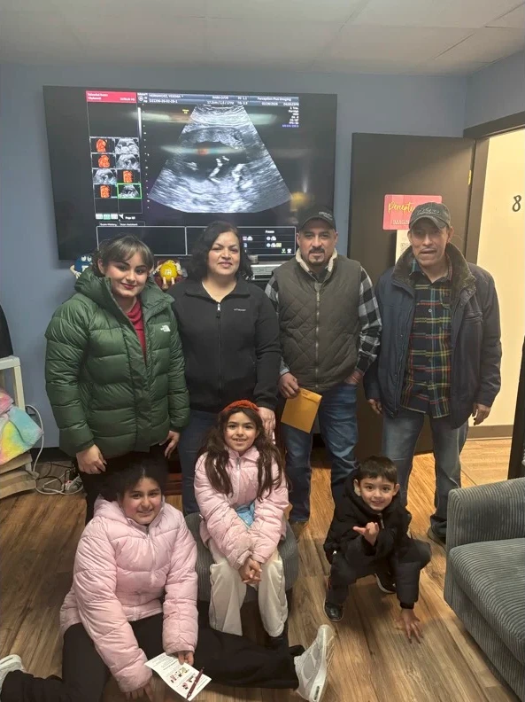 A family with young children gathered in the studio, their scan on the screen behind them.